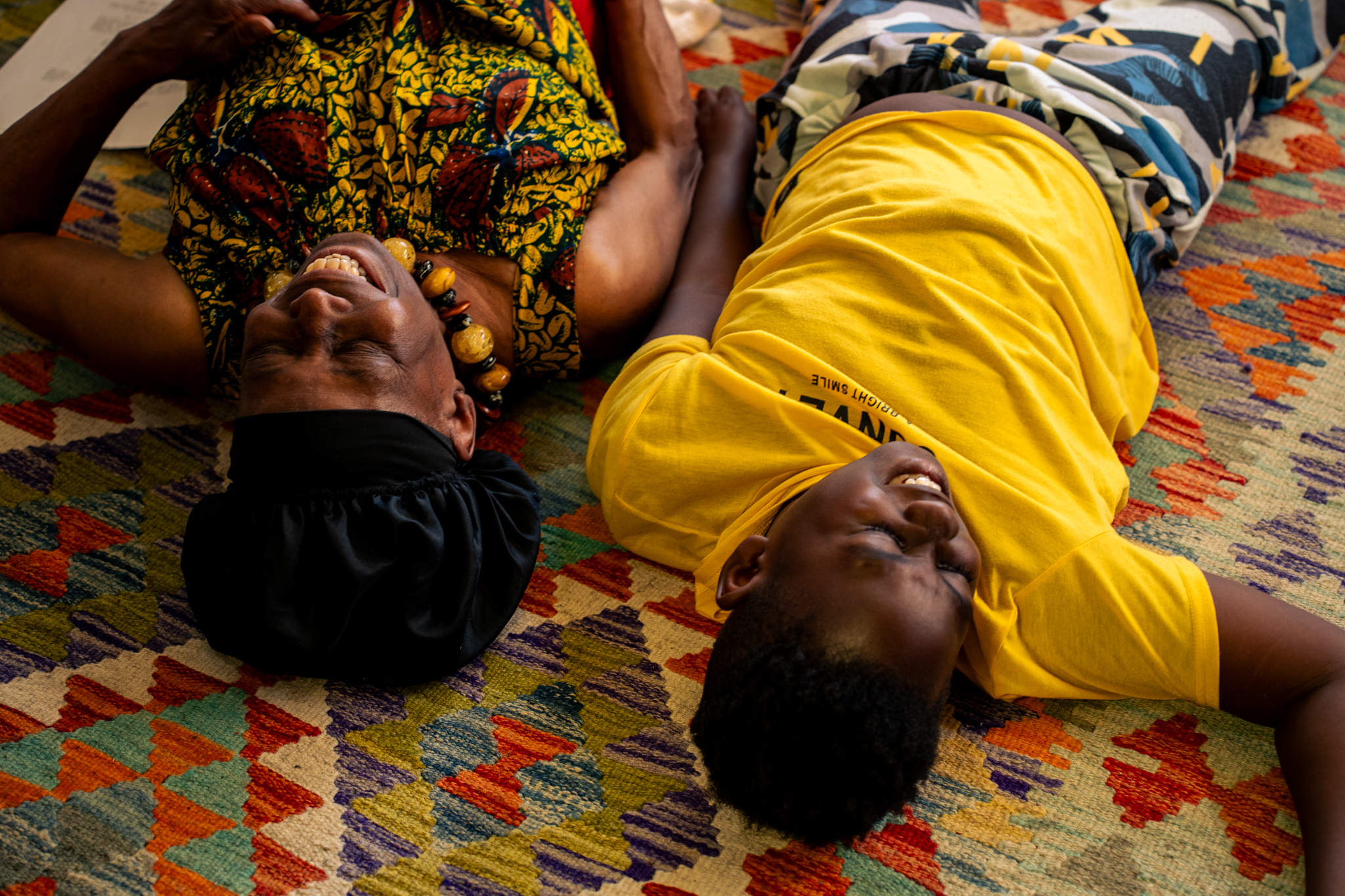 Two people lie on the floor laughing, an older lady on the left and a young boy on the right